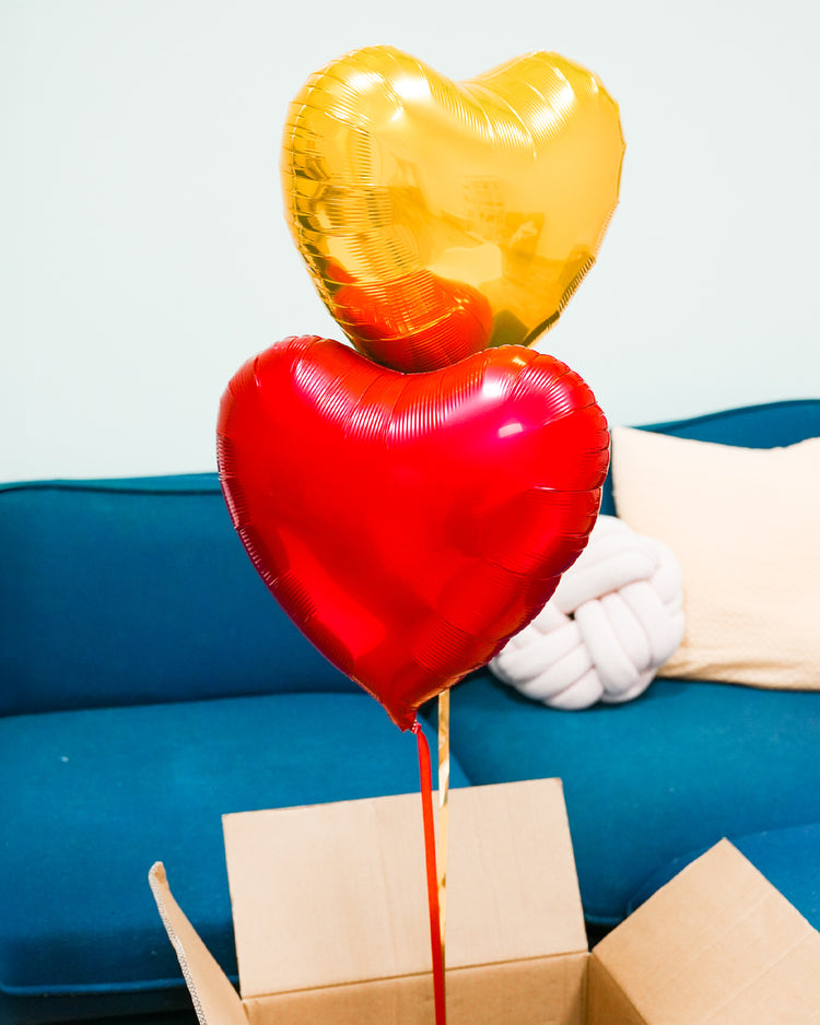 Box contenant deux ballons en forme de cœur rouge et or.