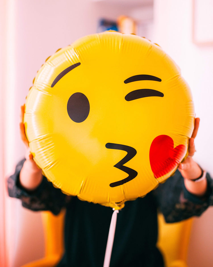 Ballon Emoji Bisous en forme de coeur rouge avec un visage souriant, idéal pour exprimer l'amour et la tendresse.