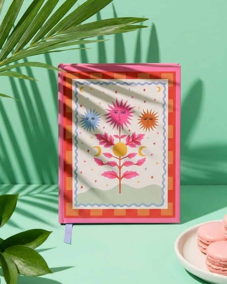 Carnet avec motif soleil sur fond hot pink, ouvert sur une table