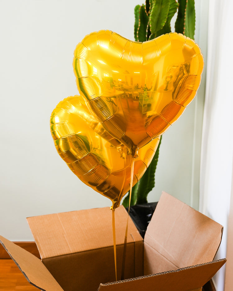 Box contenant deux ballons en forme de cœur dorés.
