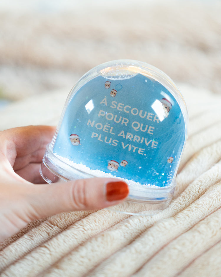 Boule à neige avec flocons scintillants et décor festif.