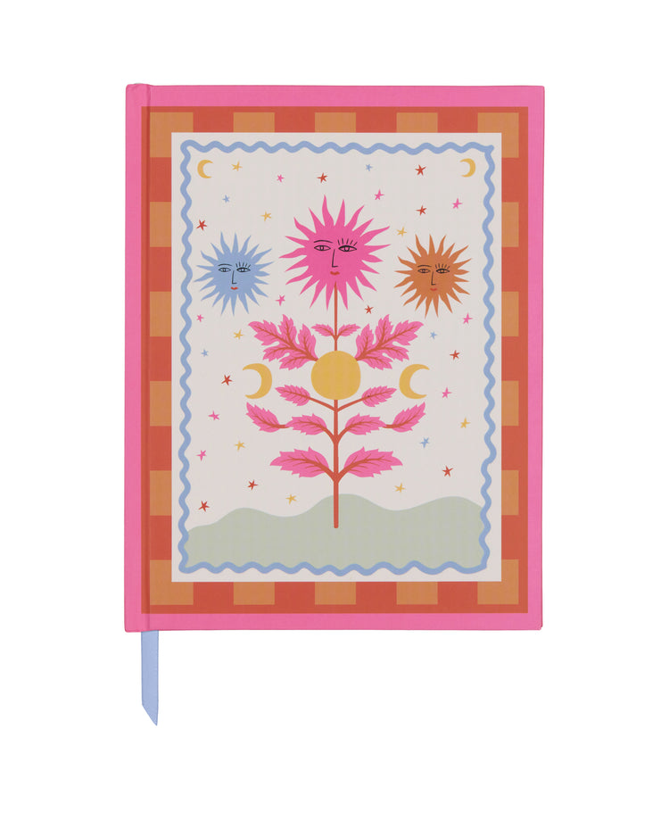 Carnet avec motif soleil sur fond hot pink, ouvert sur une table