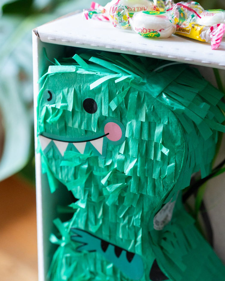 Piñata dinosaure colorée avec bonbons visibles à l'intérieur.